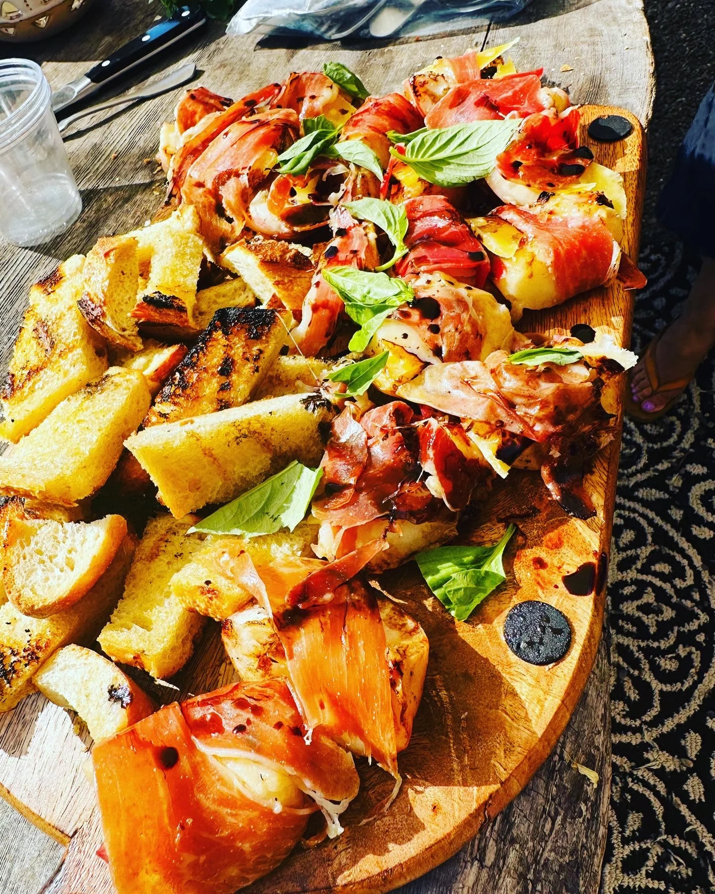 A platter of peaches, burrata, tomatoes, greens, and sliced bread