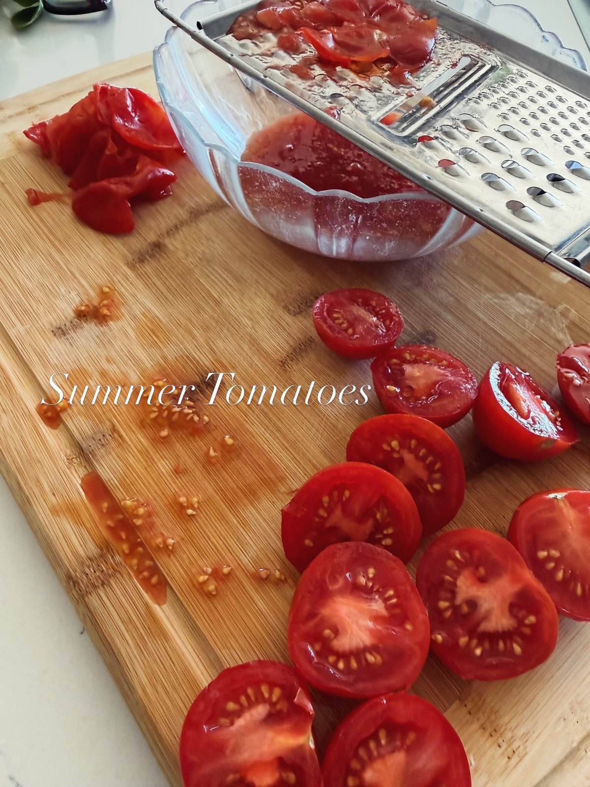 Halved ripe summer tomatoes on a wooden board beside a grater and a bowl of grated tomato