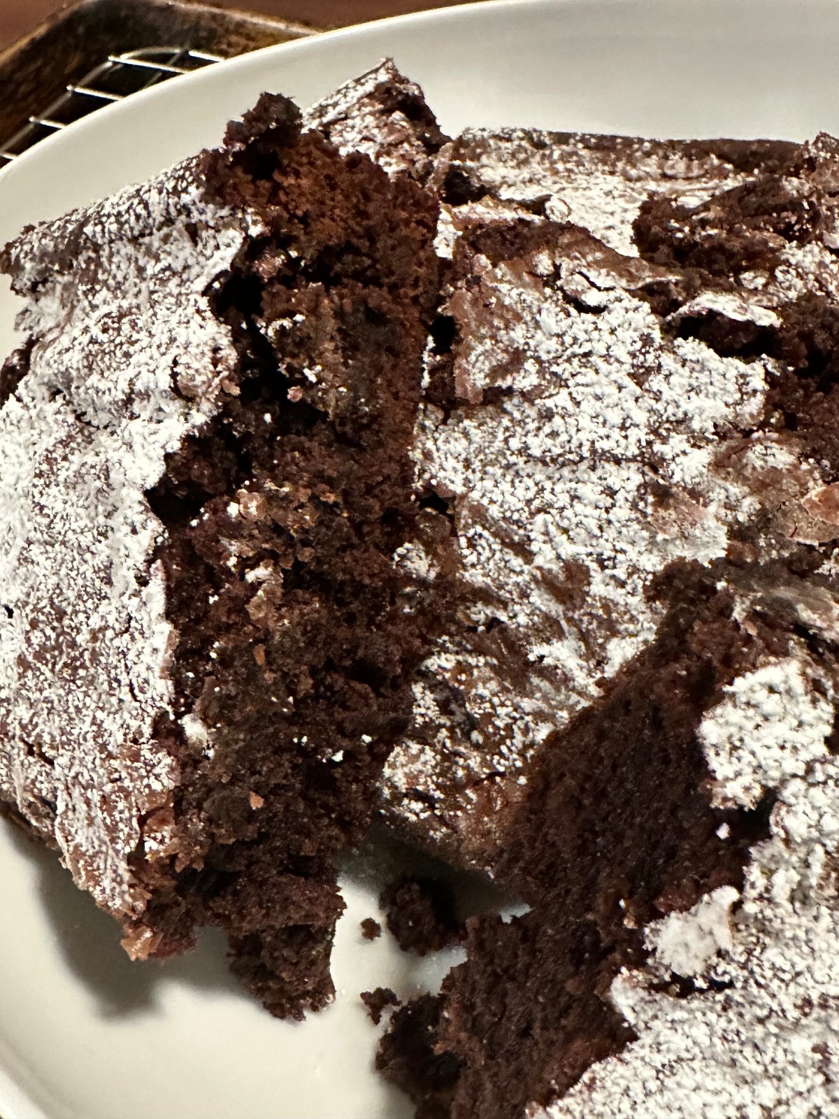 A slice of dark chocolate cake dusted with powdered sugar on a white plate