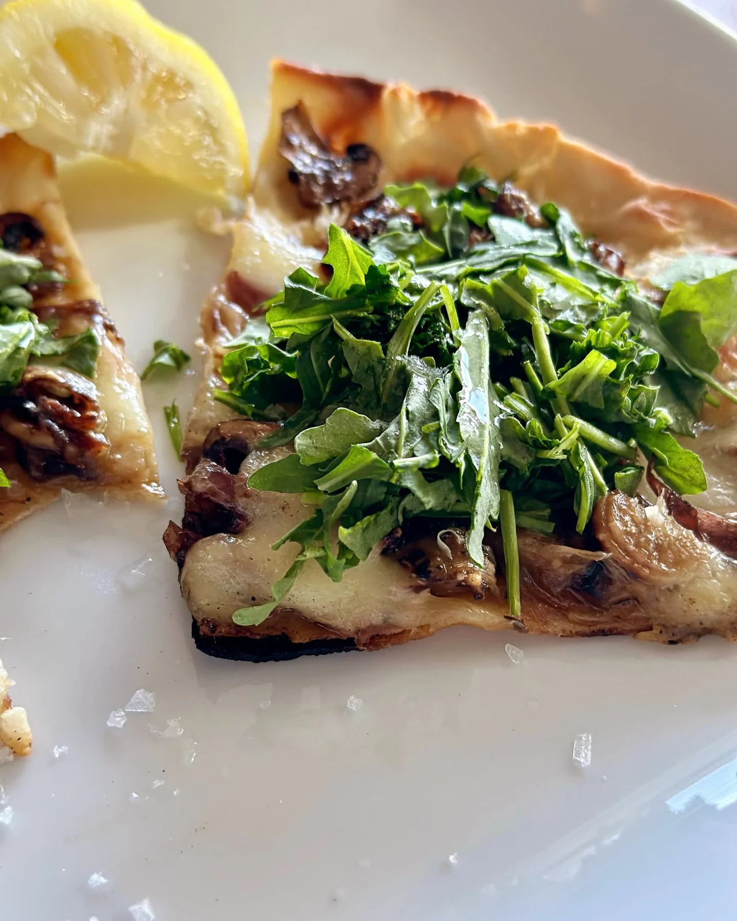 A slice of mushroom pizza topped with fresh greens on a white plate
