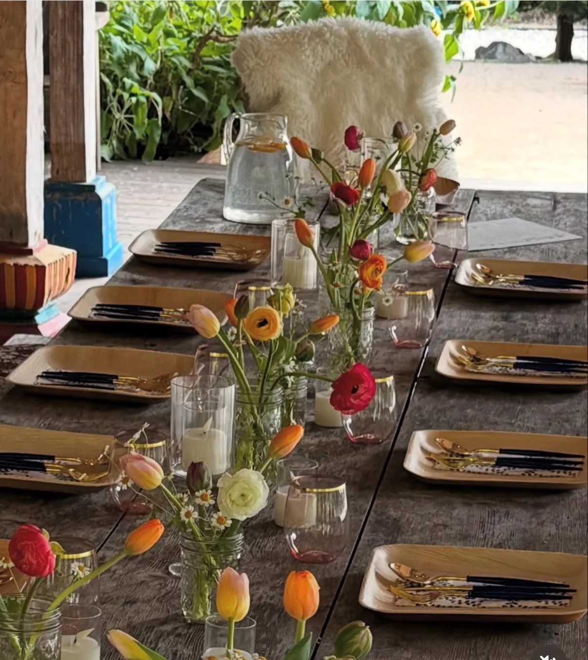 A long rustic table with individual wildflowers, candles, amber plates, and pink glasses