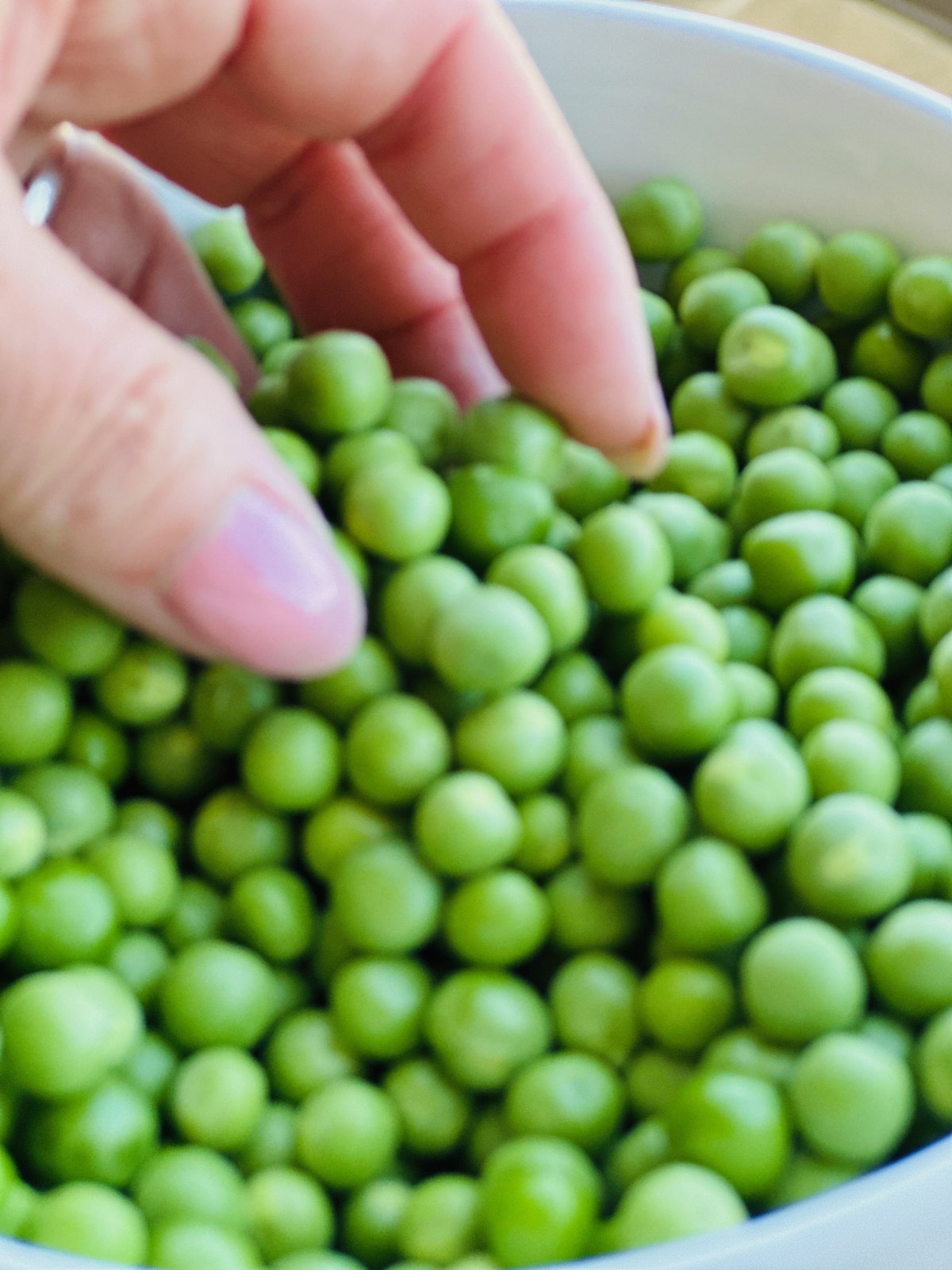 A hand reaching into a bowl of freshly shelled green peas