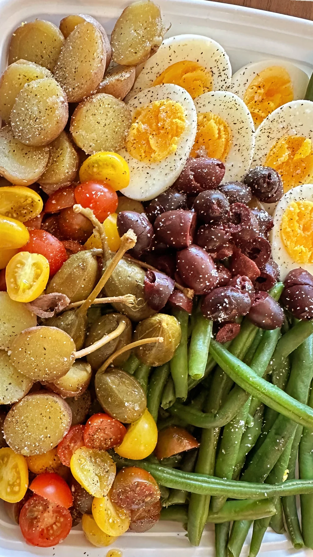 A Niçoise-style platter with halved eggs, green beans, potatoes, tomatoes, olives, and sliced vegetables
