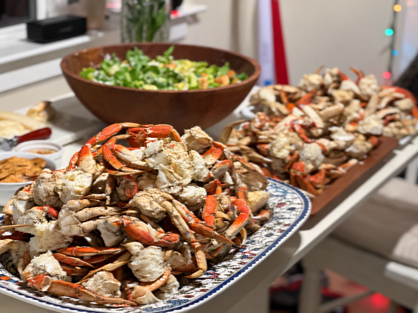 Two large platters piled with cooked crab beside a wooden bowl of salad for a celebration.