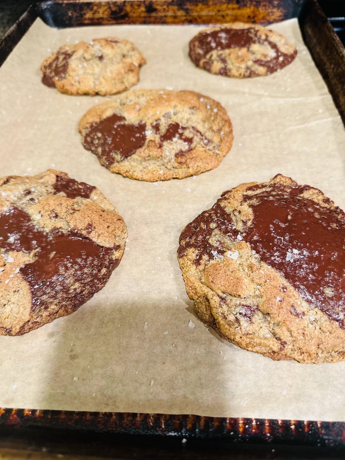 Freshly baked chocolate chunk cookies topped with flaky salt on a parchment-lined baking sheet