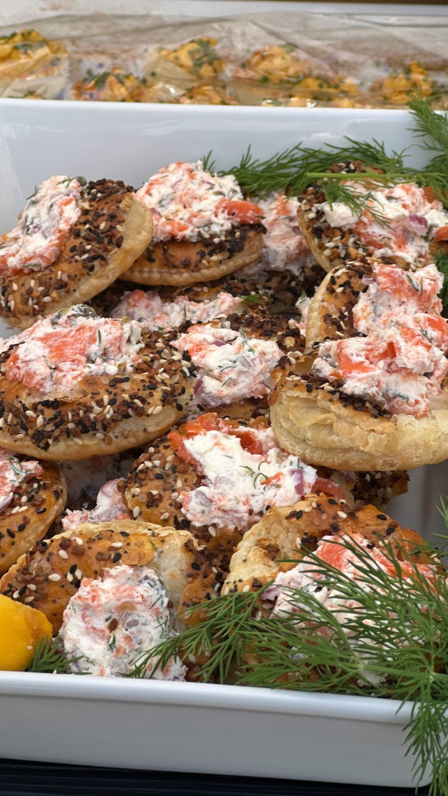 A white tray of everything-seasoned puff pastry rounds with smoked salmon cream cheese and fresh dill