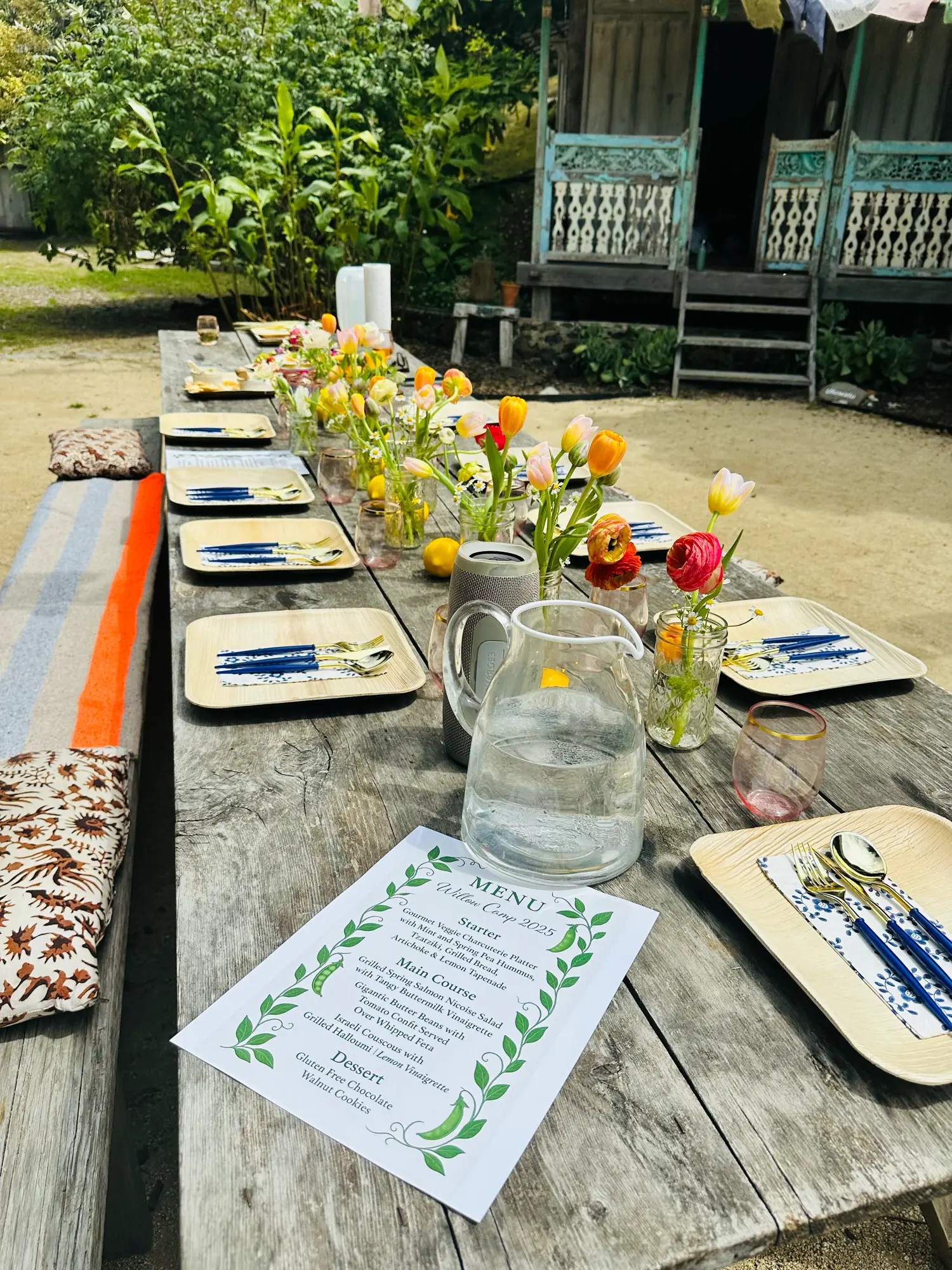An outdoor wooden table set with tulips, colorful glassware, plates, and a printed menu