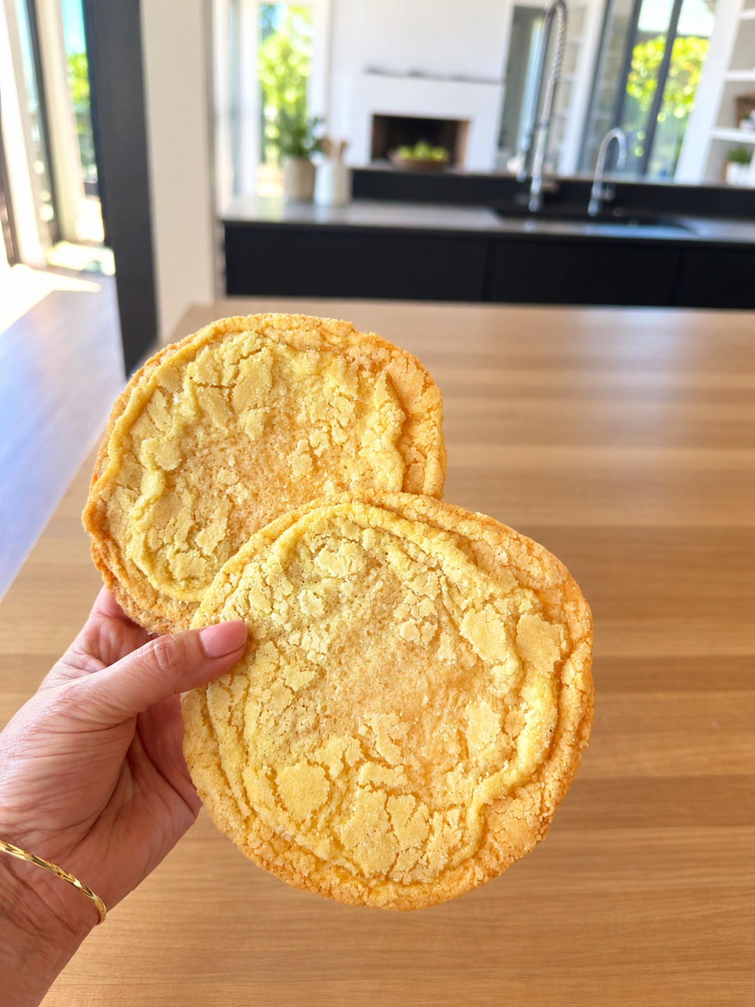 Two large golden sugar cookies held in one hand against a bright, uncluttered kitchen background.