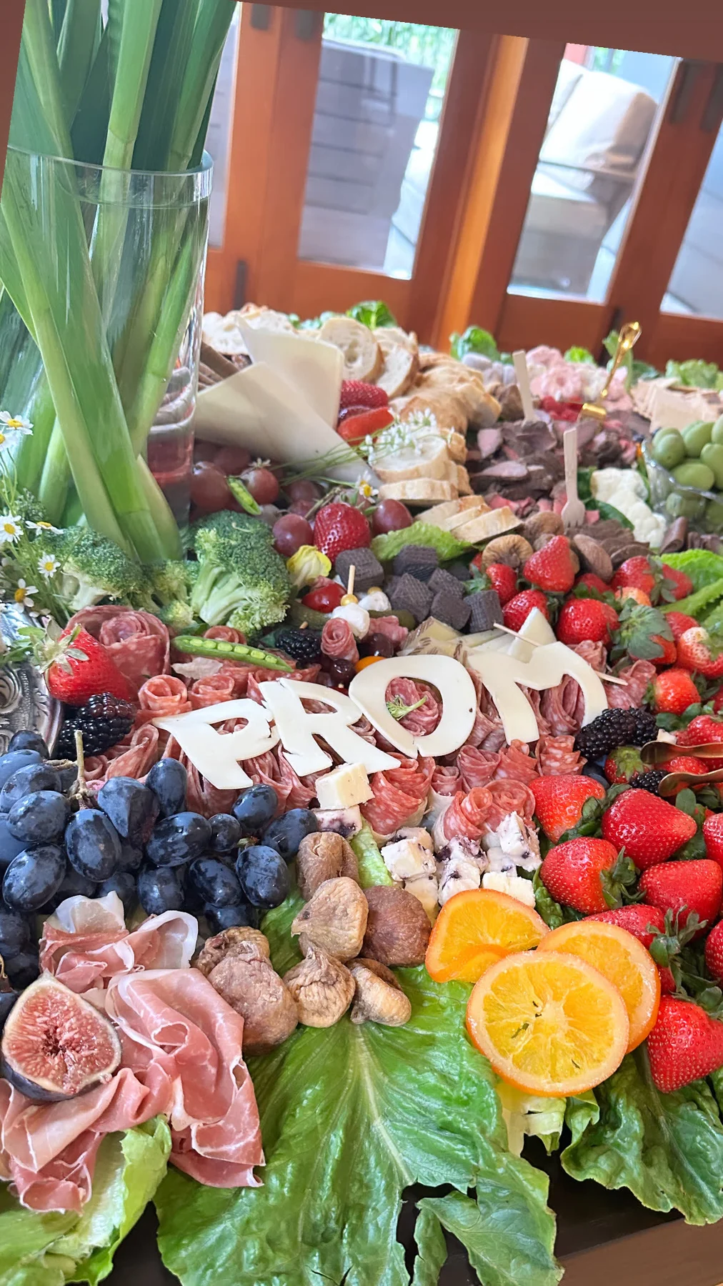 A long prom grazing table filled with fruit, cheese, charcuterie, flowers, and white PROM letters