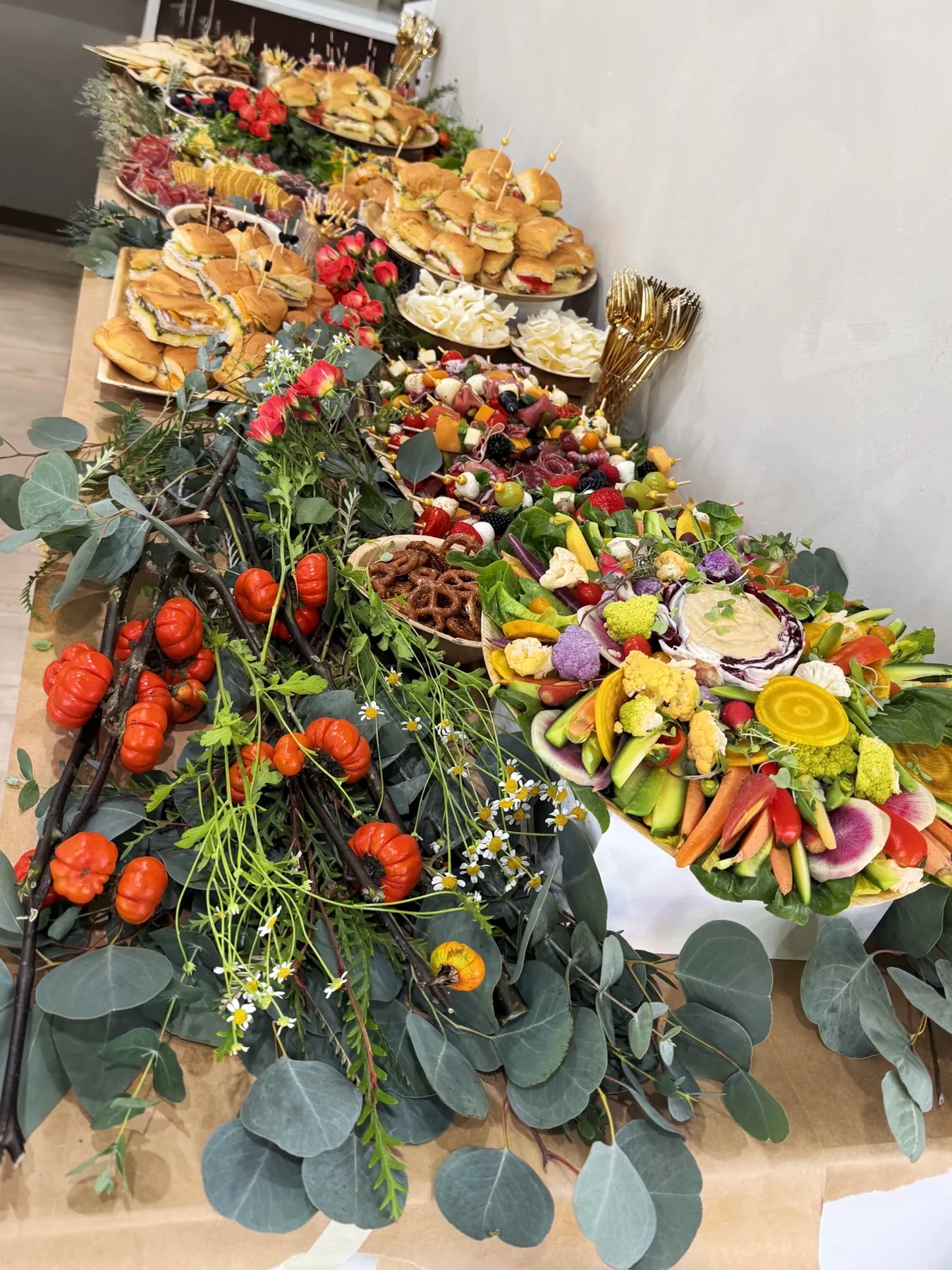 A long grazing table with eucalyptus, tomatoes, citrus, charcuterie, cheese, vegetables, and flowers
