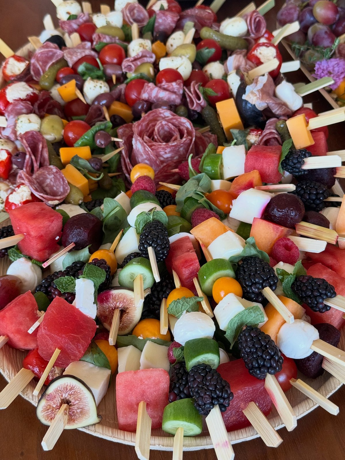 Skewers of watermelon, blackberries, figs, mozzarella, and cured meats arranged around a salami rose