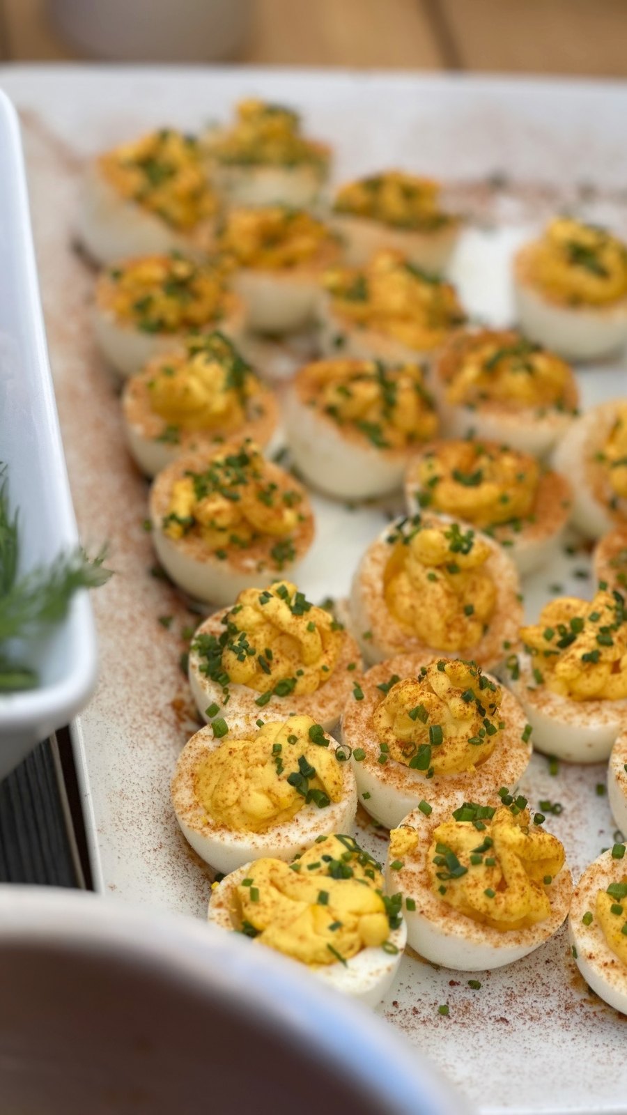 Deviled eggs piped with yolk filling, dusted with paprika, and topped with chives on a white platter