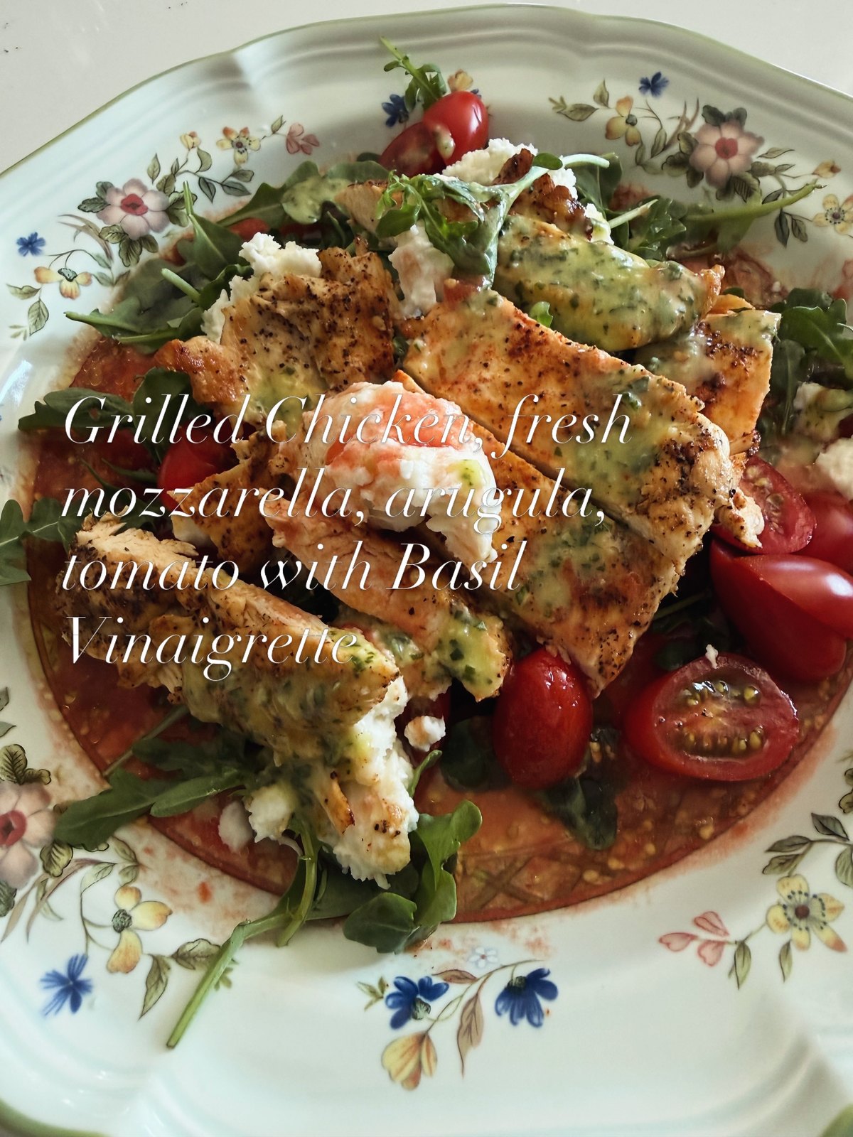 Sliced grilled chicken over arugula with fresh mozzarella, tomatoes, and basil vinaigrette on a floral platter