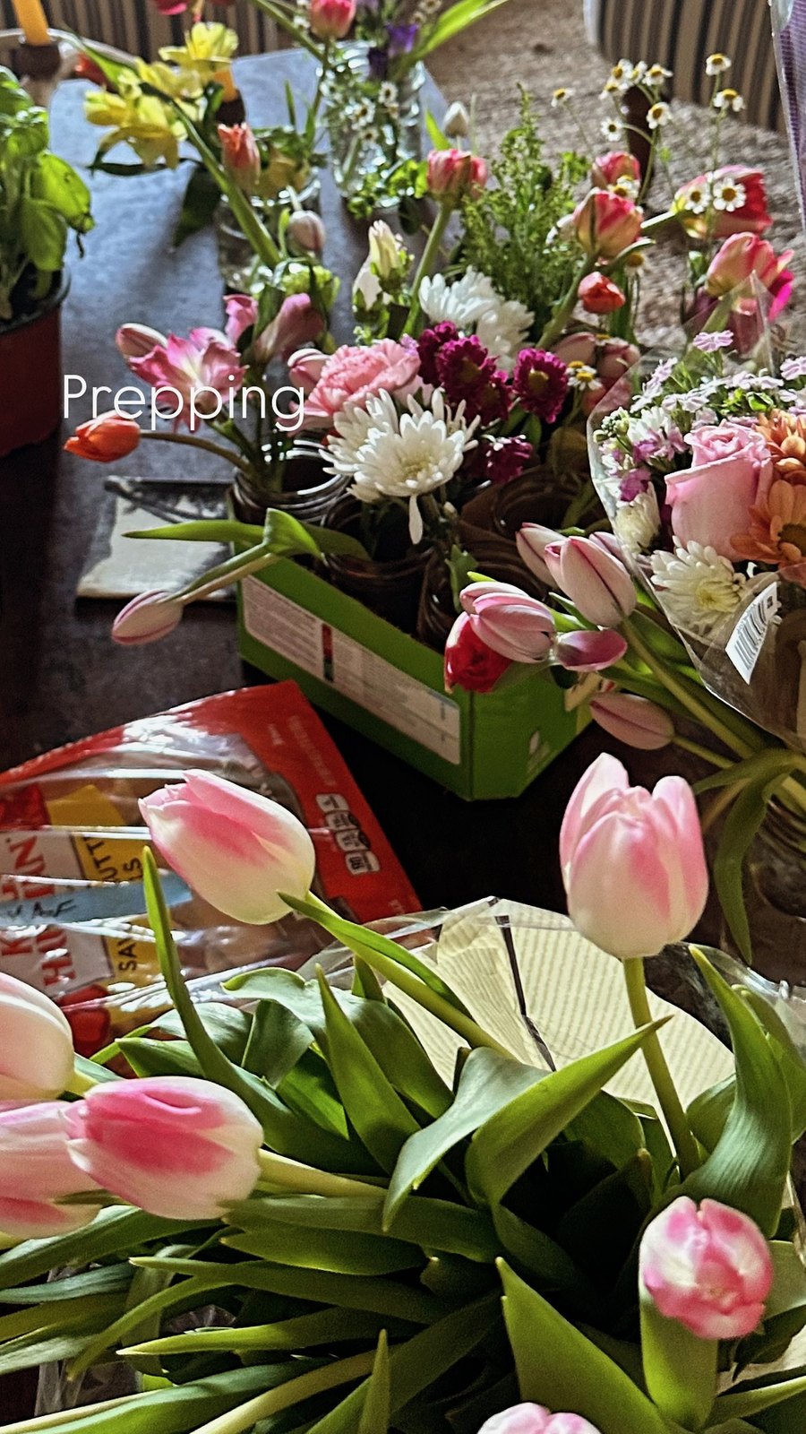Bunches of tulips, roses, daisies, and chamomile waiting on a table before being arranged