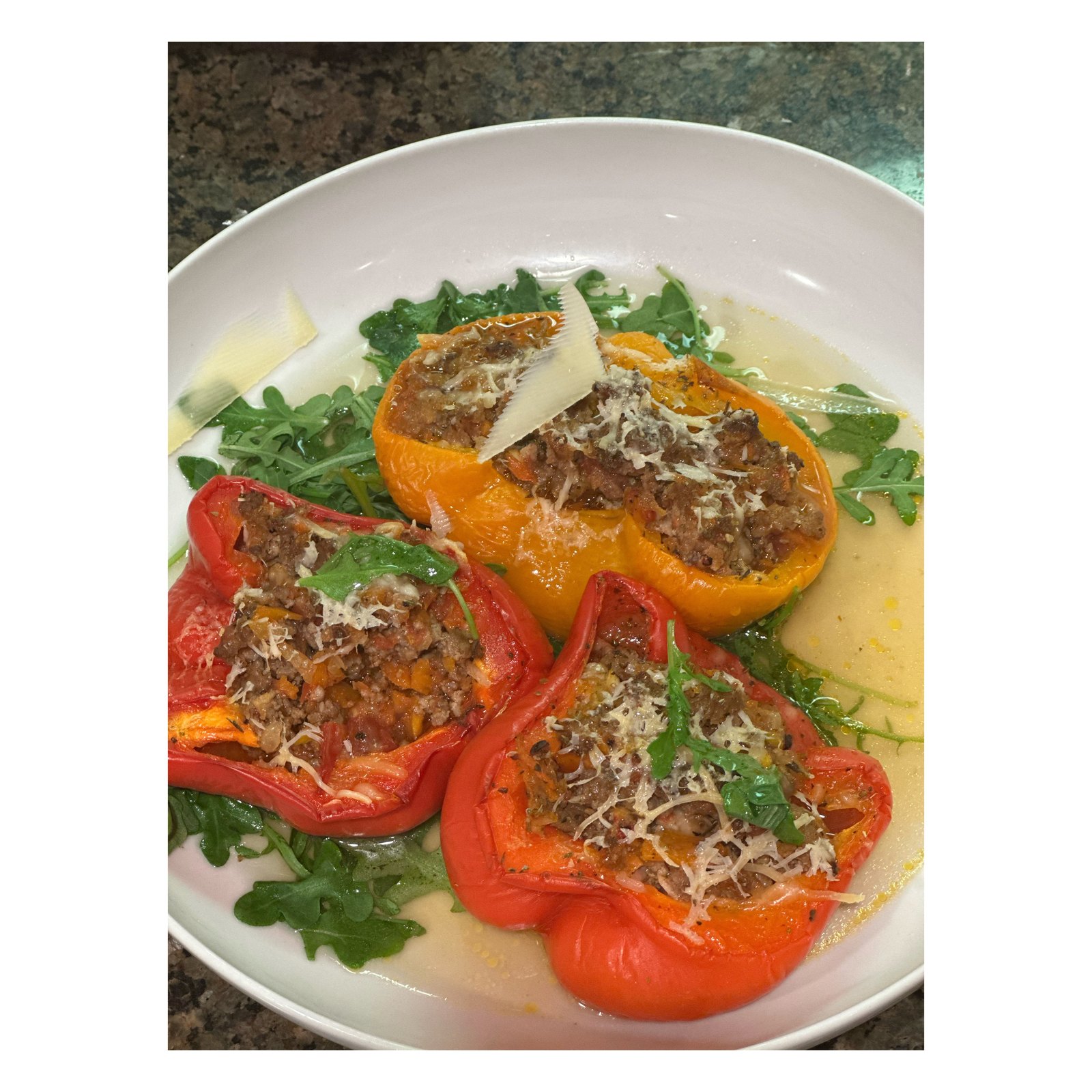 Red and yellow stuffed peppers with melted cheese over arugula in a white bowl