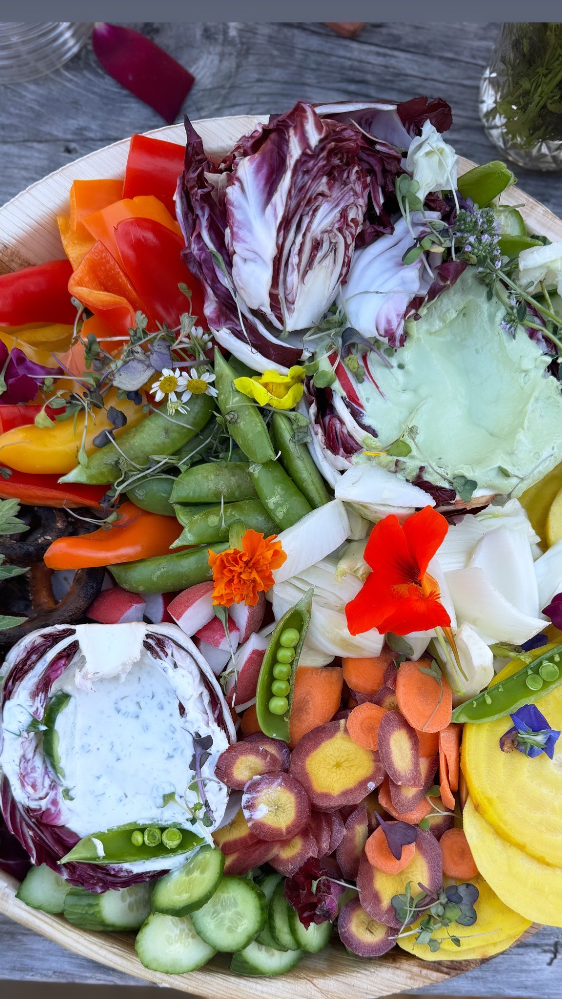 A vivid vegetable board with radicchio, peppers, peas, carrots, cucumber, edible flowers, and herb dip
