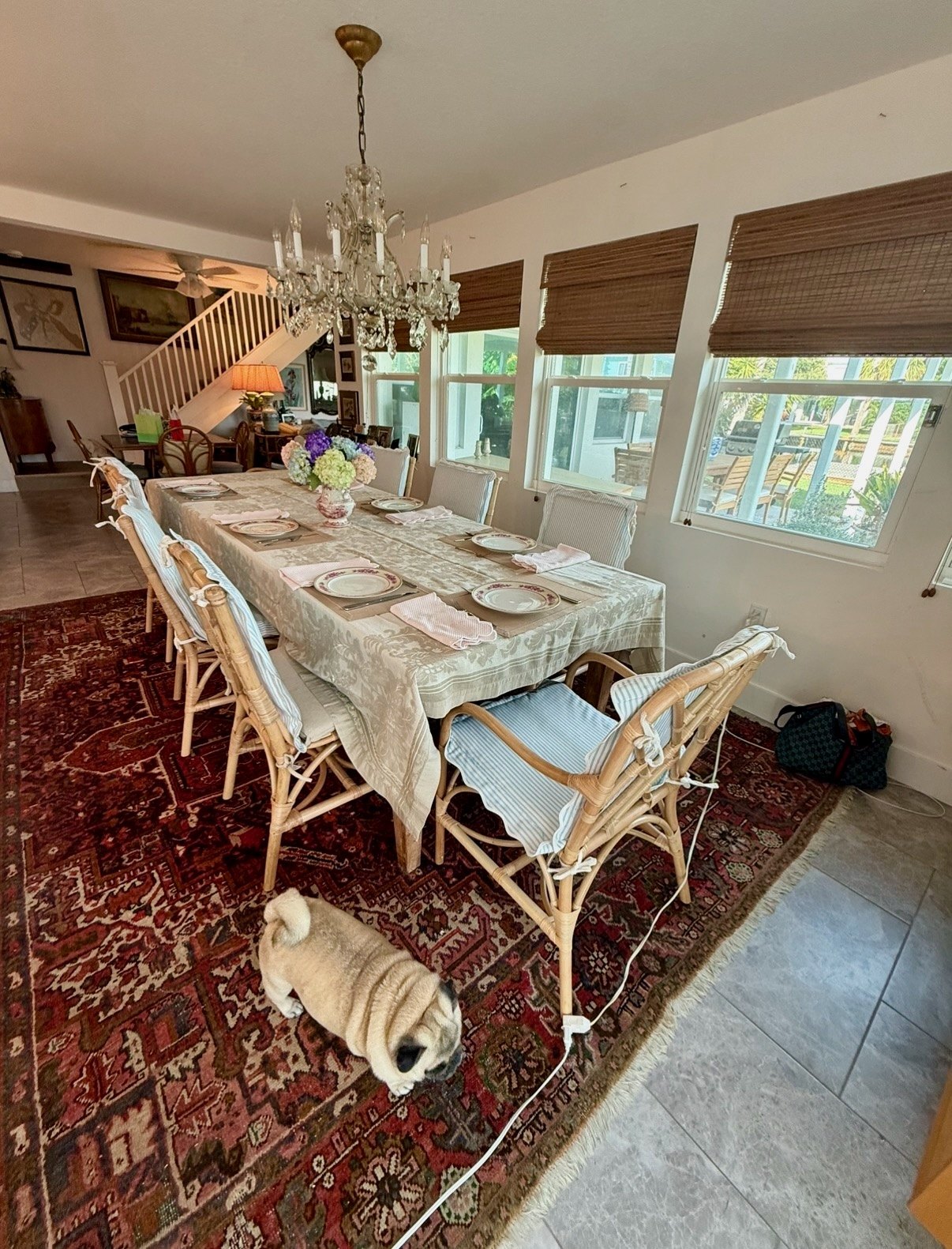 A long dining table set with patterned linens and a vase of hydrangeas beneath a chandelier
