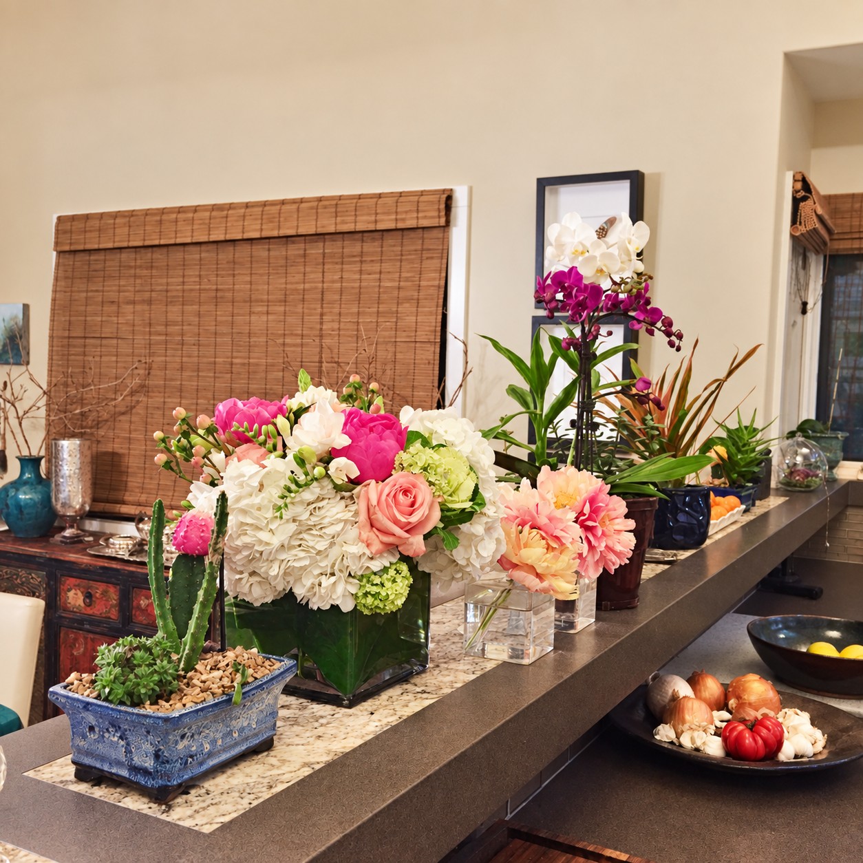 Pink and white flowers arranged beside white and purple orchids and potted plants on a kitchen counter.