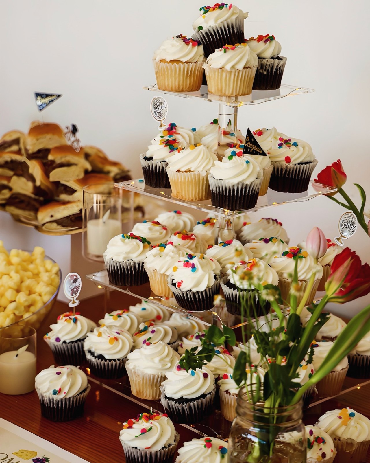 A tiered stand of sprinkled cupcakes with graduation picks, sandwiches, and tulips