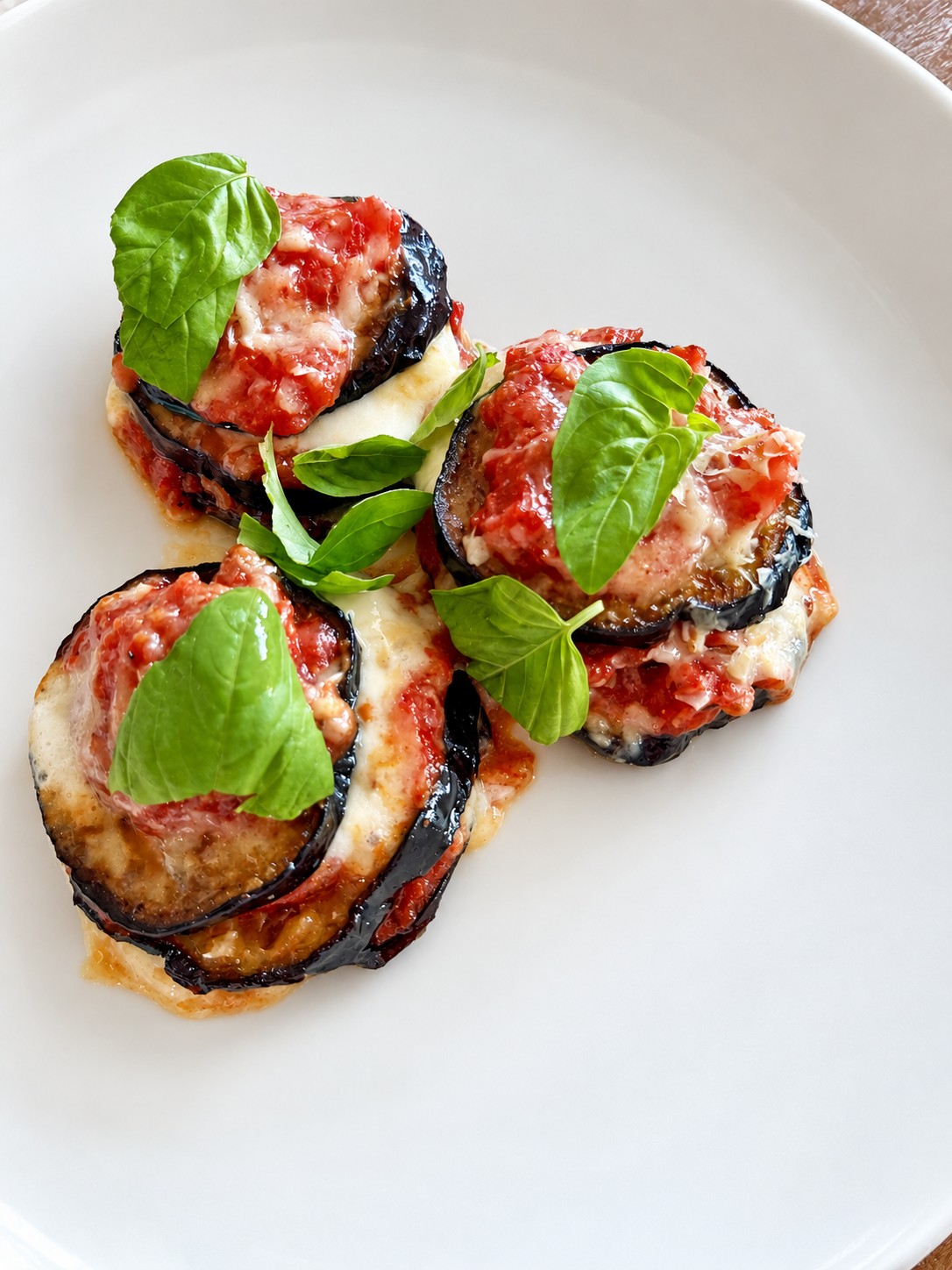 Stacks of roasted eggplant, tomato sauce, and melted cheese topped with fresh basil on a white plate.